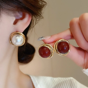 Detail of vintage round pearl earrings with golden wire wrap in white and deep red colors
