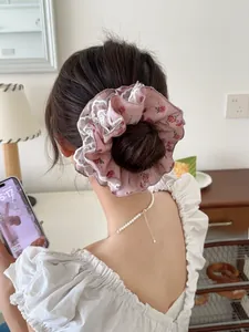 Détail d'un chouchou rose à fleurs et dentelle porté sur un chignon en intérieur