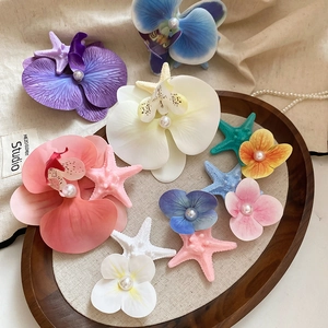 Detailed view of starfish and orchid hair clips with pearls on a wooden tray