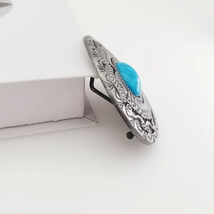 Side close-up of vintage silver belt buckle with embossed patterns and oval turquoise stone
