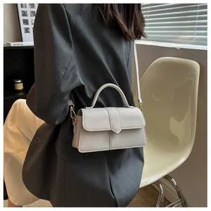 Détail d'un sac à main beige en cuir avec ferrures dorées et coutures géométriques sur modèle