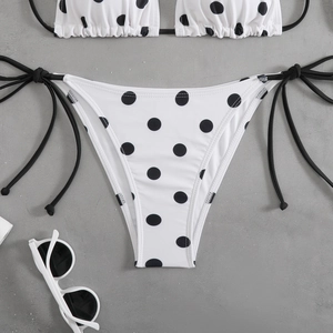 Detailed view of white polka dot bikini bottom with adjustable black side ties on concrete