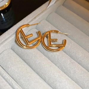 Macro shot of gold-plated metal letter E earrings on a grey velvet jewelry display tray