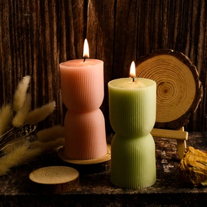 Dettaglio di candele geometriche a righe accese con forma a clessidra su legno
