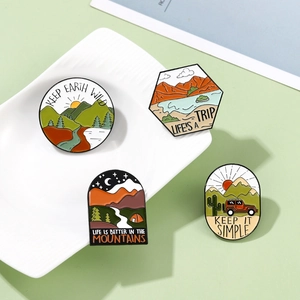 Outdoor adventure enamel pins set featuring mountains, forest and camping motifs on a tray