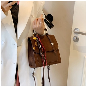 Detalle del bolso bandolera marrón vintage con asa metálica y colgante de llave dorada