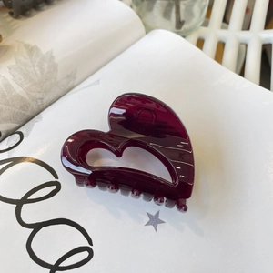 Gros plan d'une pince à cheveux en forme de cœur rouge foncé brillant sur un livre