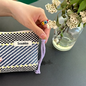 Detail of woven cosmetic bag with geometric waves, yellow stitching, and purple zipper pull