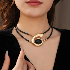 Close-up of a layered black leather necklace with a gold oval pendant and black gemstone