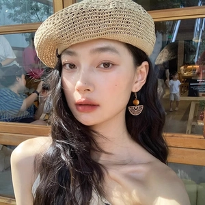 Ethnic fan-shaped cutout earrings with dark brown wood beads worn by a model in a cafe