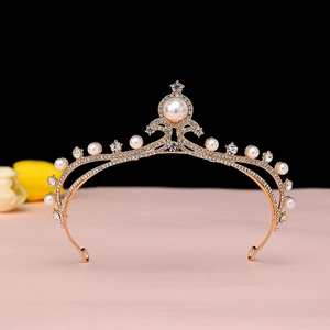 Detail view of baroque gold crown featuring white pearls and crystals on black background