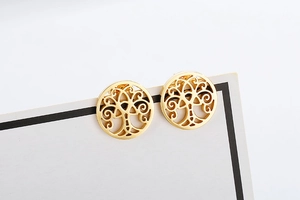 Close-up of golden hollow tree of life earrings on white display card with metal texture