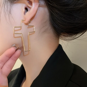 Gros plan d'un modèle portant des boucles d'oreilles croix évidées en métal doré poli
