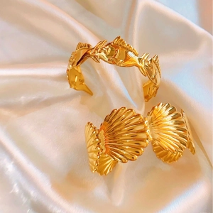Elegant gold open cuff bracelets with tropical fish and seashell motifs on white satin