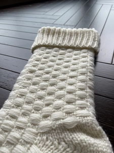 Close-up of white knitted Christmas stocking with 3D square texture on dark wood background