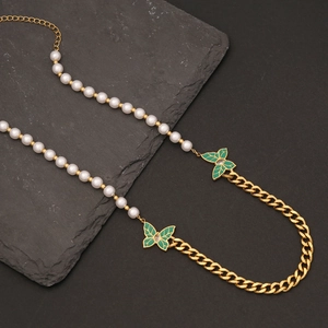 Gros plan d'un collier doré avec perles blanches et pendentifs papillons verts sur pierre