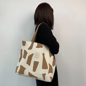 Canvas tote bag with geometric patterns shown on shoulder against a minimalist white wall
