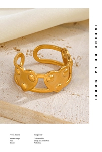 Détail d'une bague à rivets cœur doré présentant plusieurs cœurs sur texture pierre beige