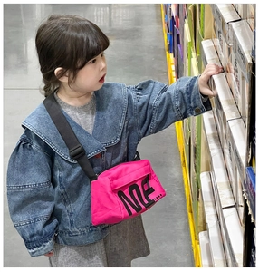Détail d'un sac bandoulière en toile rose vif avec lettrage noir porté par une fillette