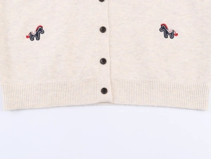 Detailed close-up of cream knit cardigan featuring embroidered pony accents and wood buttons