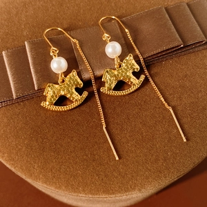 Detailed close-up of golden rocking horse earrings with pearls on brown velvet