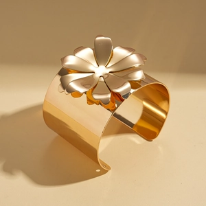 Gros plan d'un large bracelet manchette en métal doré avec une grande fleur 3D polie