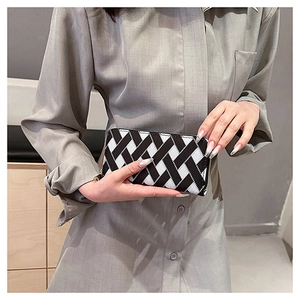 Detail of hand holding a black and white woven patterned long clutch with a metal zipper