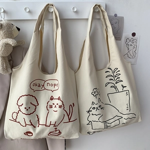 Detail of two cream white canvas tote bags featuring cute cat and dog cartoon illustrations