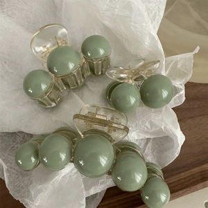 Detailed view of three transparent green pearl hair claws on white silk paper