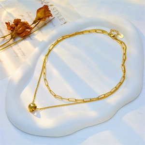 Double-layered gold chain necklace with a faceted geometric bead pendant on a white tray
