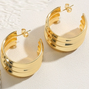 Macro view of wide gold-plated twist earrings with a glossy metallic finish and texture