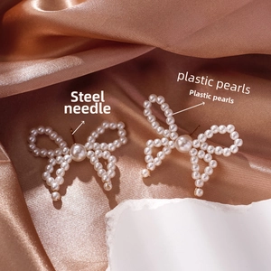 Close-up of bow earrings with faux pearls on bronze silk and stone backdrop