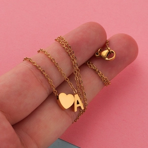 Detail of a gold stainless steel necklace with a heart pendant and letter A charm