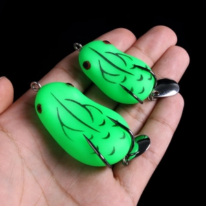 Macro shot of two green frog lures with double hooks and metal sequins in a hand