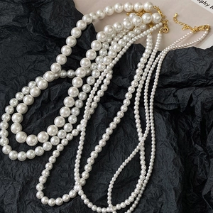 Three elegant white pearl necklaces with gold clasps on a textured black paper backdrop