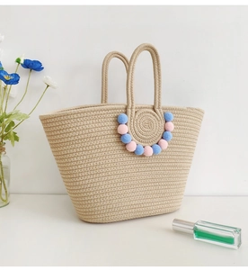 Detail of beige woven tote bag with decorative pink and blue pompoms on a white surface