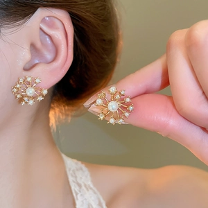 Close-up of golden snowflake stud earrings with pearls and zircons worn by a model