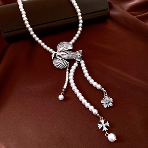 Close-up of vintage pearl necklace with silver swallow pendant on red silk background