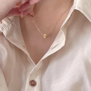 Detail of a gold bead pendant necklace worn by a model over a white cotton shirt