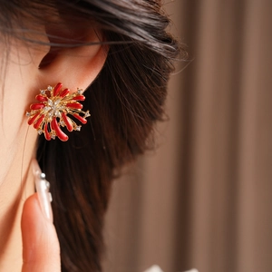 Detail of red and gold firework-shaped stud earrings with sparkling crystals on a model
