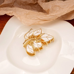 Detail of leaf-shaped gold hair claw clip with white enamel finish on ceramic tray