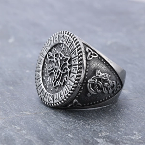 Vintage stainless steel Viking wolf head ring with Norse runes on a grey stone background