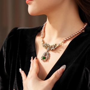 Close-up of vintage pearl necklace featuring gold leaf accents and a green gemstone pendant