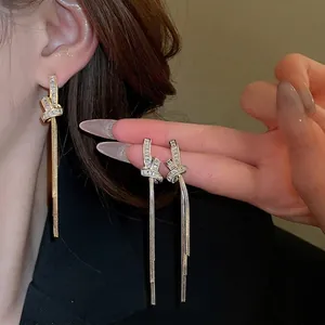 Elegant gold-plated knot tassel earrings with sparkling zircon crystals on a model's ear