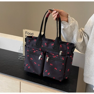 Detail of black nylon tote bag featuring cherry print and multiple front zipper pockets