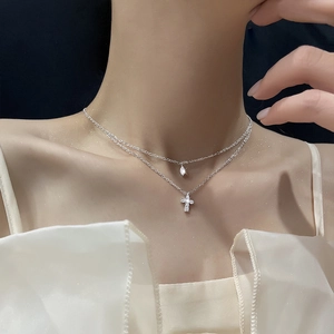 Close-up of double layered silver cross necklace with teardrop zircon pendant on neck