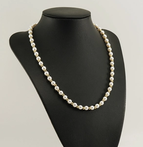 Détail d'un collier de perles blanches et billes dorées sur un buste de mannequin