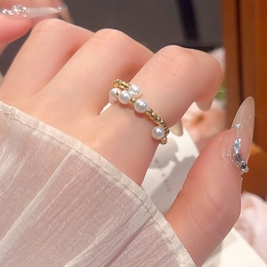 Detail of stacked gold beaded ring featuring white pearls on a model hand with ruffles