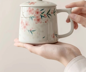 Close-up of hand-held peach blossom ceramic mug with lid and hand-painted floral details
