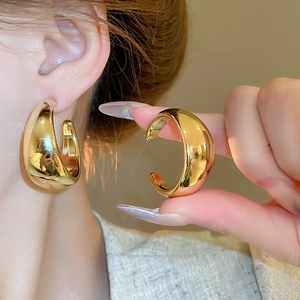 Macro detail of glossy gold C-shape chunky earrings with high-polished mirror finish